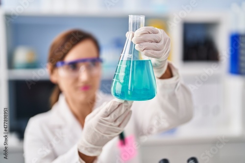 Middle age woman wearing scientist uniform measuring liquid at laboratory