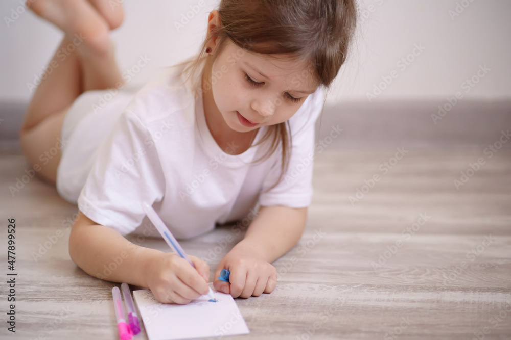 Homeschooled girl, draws in a notebook lying on the floor, dressed in a white T-shirt. High quality photo Homeschooled girl, draws in a notebook lying on the floor, dressed in a white T-shirt. High quality photo