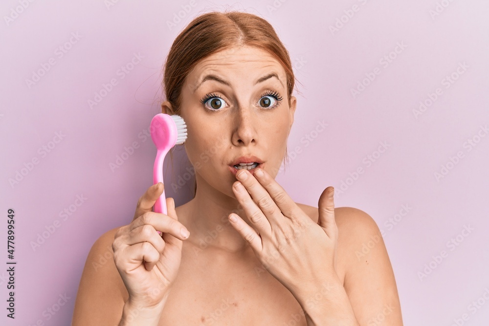 Young irish woman using facial exfoliating brush covering mouth with hand, shocked and afraid for mistake. surprised expression Young irish woman using facial exfoliating brush covering mouth with hand, shocked and afraid for mistake. surprised expression