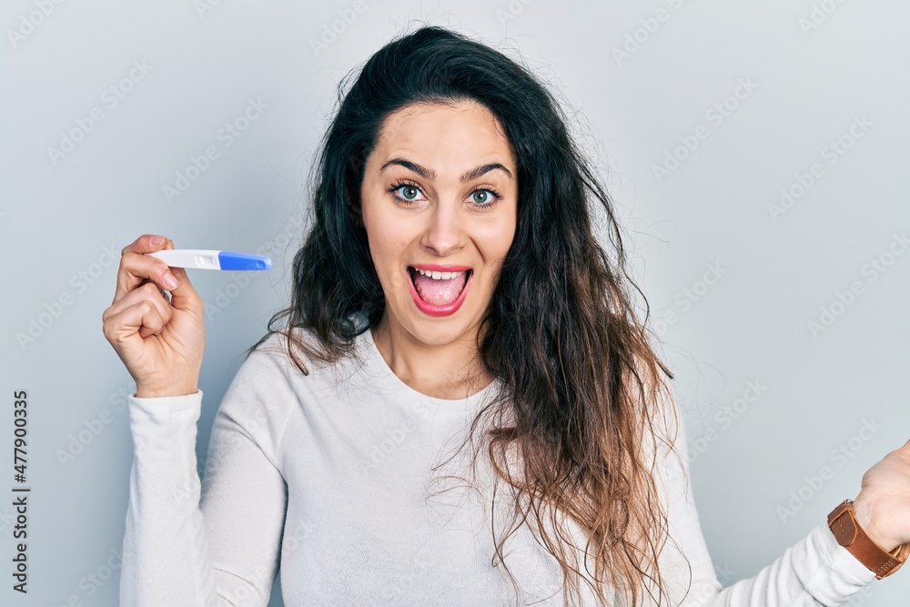 Young hispanic woman holding thermometer celebrating achievement with happy smile and winner expression with raised hand Young hispanic woman holding thermometer celebrating achievement with happy smile and winner expression with raised hand