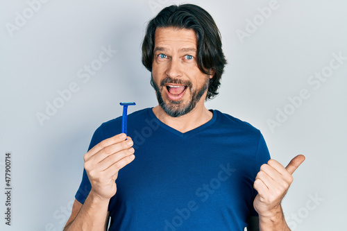 Middle age caucasian man holding razor pointing thumb up to the side smiling happy with open mouth