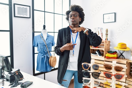 African young woman working as manager at retail boutique cutting throat with hand as knife, threaten aggression with furious violence