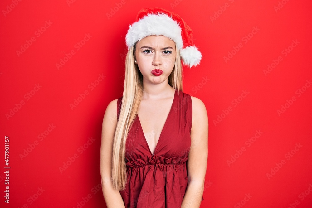Young blonde girl wearing christmas hat puffing cheeks with funny face. mouth inflated with air, crazy expression. Young blonde girl wearing christmas hat puffing cheeks with funny face. mouth inflated with air, crazy expression.