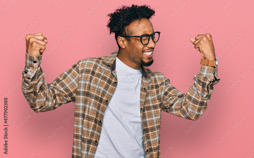 Fototapeta premium Young african american man with beard wearing casual clothes and glasses very happy and excited doing winner gesture with arms raised, smiling and screaming for success. celebration concept.