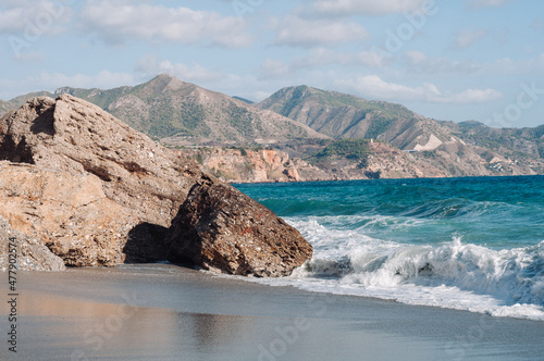 Aerial top view of sea waves hitting rocks on the beach with turquoise sea water.  photo