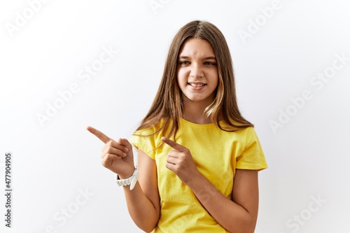 Young brunette teenager standing together over isolated background pointing aside worried and nervous with both hands  concerned and surprised expression