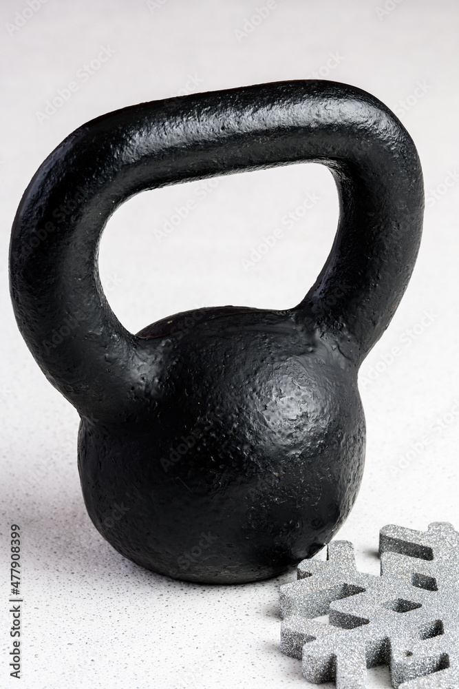 Fototapeta premium Kettlebell winter fitness, black kettlebell on a white background with silver sparkles and a silver snowflake