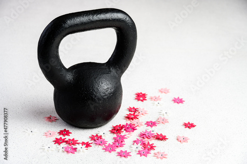 Fototapeta Naklejka Na Ścianę i Meble -  Kettlebell spring fitness, black kettlebell on a white background with silver sparkles and red, pink, and white flowers
