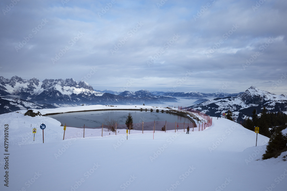 Kirchberg, Austria - December 26, 2021: Ski resort Kitzski in the Alps. Mountain snowy peaks, alpine village. Water pond