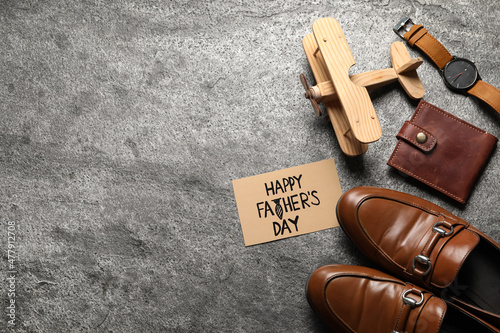 Card with phrase Happy Father's Day, shoes, toy plane and men accessories on grey background, flat lay. Space for text