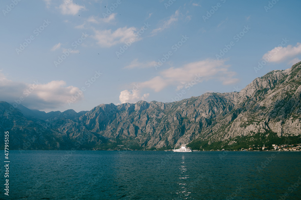 White yacht sails on the Bay of Kotor against the backdrop of a mountain range