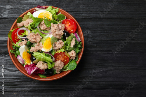 Bowl of delicious salad with canned tuna and vegetables on black wooden table, top view. Space for text