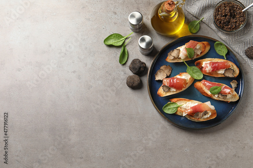 Delicious bruschettas with cheese, prosciutto and slices of black truffle on grey table, flat lay. Space for text