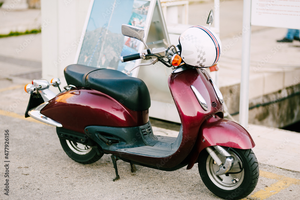 Burgundy motor scooter with a white helmet stands on the street