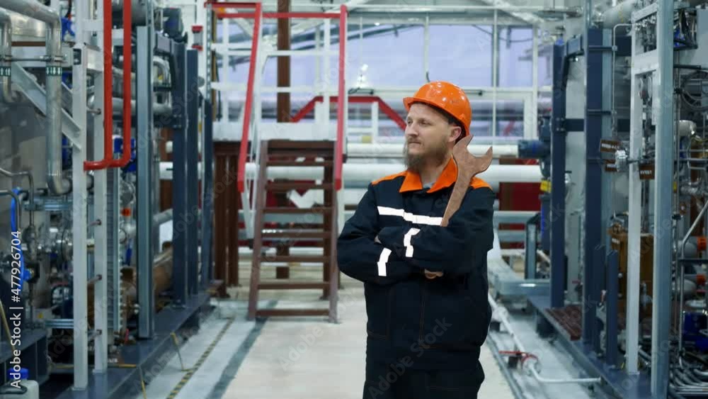 A plant worker in a helmet with a wrench at his workplace, an operator of technological equipment stands in a gas compression shop. Equipment for the oil and gas and chemical industries. A plant worker in a helmet with a wrench at his workplace, an operator of technological equipment stands in a gas compression shop. Equipment for the oil and gas and chemical industries.