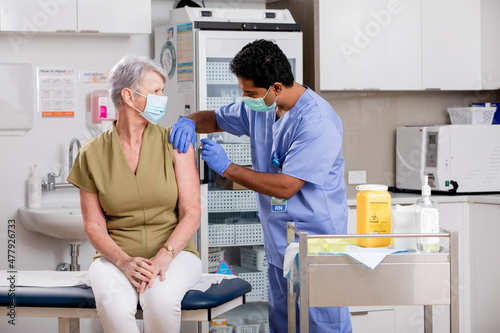 Foto A Young Indian Male Medical Nurse Administering a Covid-19 Vaccine with a Syringe Needle to an Elderly Senior Female Patient Wearing Generic ID Badge, Gloves and Mask in Hospital or Health Clinic