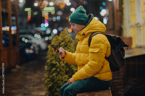 Man using smartphone sitting in a night city at winter