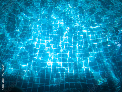 Blue swimming pool water, with waves, and reflections from sunlight, with dark shadows at the bottom of the image, late in the holidays. © sutthichai