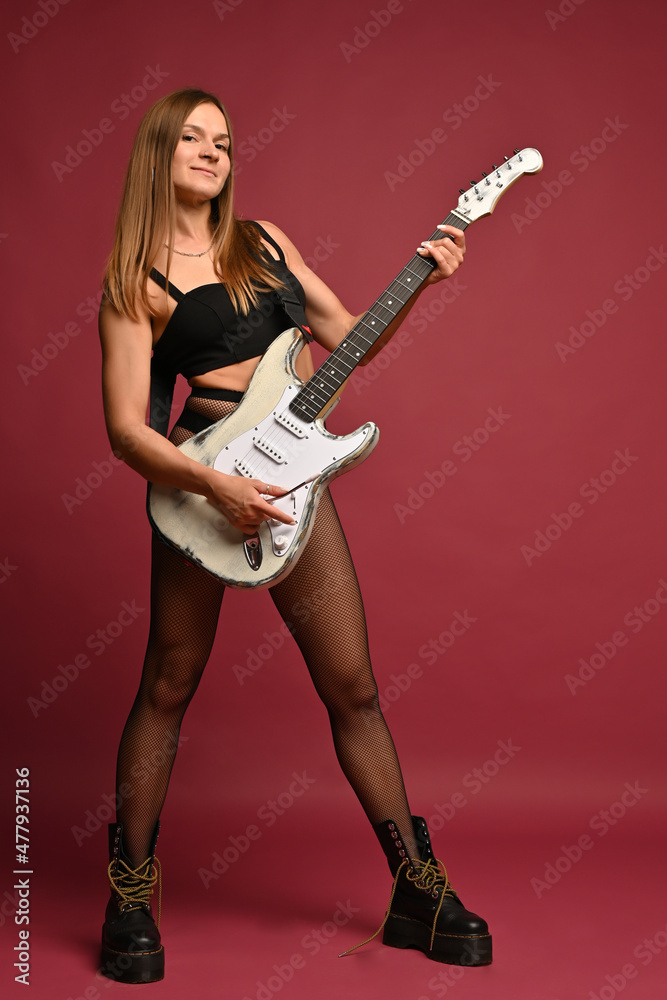 Beautiful young woman posing with guitar in studio on ruby background Beautiful young woman posing with guitar in studio on ruby background