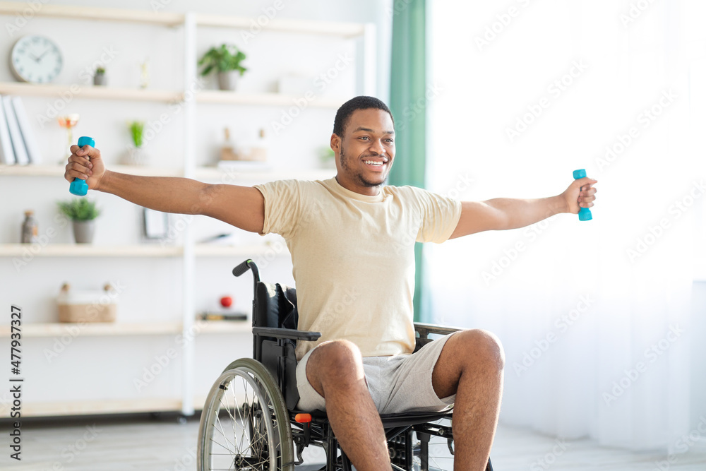 Rehabilitation workout of paraplegic people. African American man in wheelchair training with dumbbells at home Rehabilitation workout of paraplegic people. African American man in wheelchair training with dumbbells at home