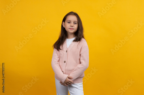 A young girl in a pink jacket and white jeans poses on a yellow background © filins