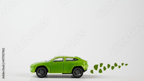 A toy green car rides over the background with an exhaust from birch leaves. The concept of reducing CO2 emissions from vehicles