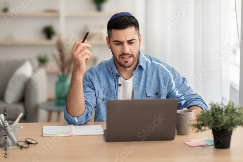 Focused israeli man working on laptop amd writing at home