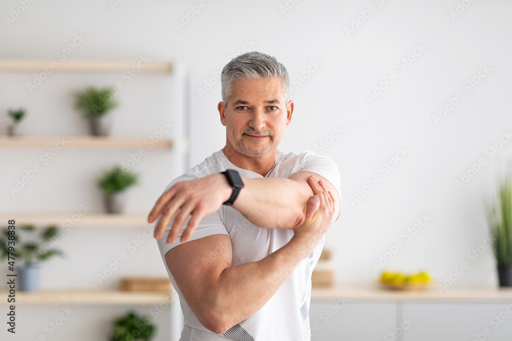Obraz premium Morning training. Active mature man warming up, stretching hands at home, training in living room interior