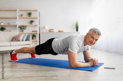 Sports and weight loss at home. Sporty mature man standing in elbow plank, strengthening his core muscles, free space