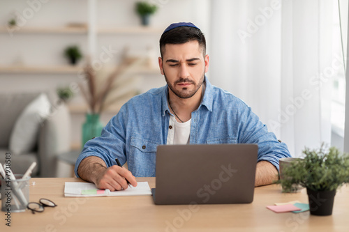 Focused israeli man working on laptop at home photo