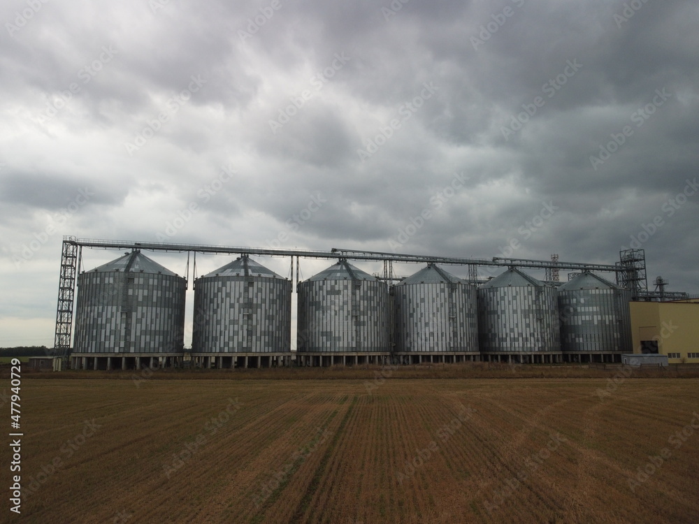 Grain elevator. Metal grain elevator in agricultural zone. Agriculture storage for harvest. Grain elevators on green nature background. Exterior of agricultural factory. Nobody. Grain elevator. Metal grain elevator in agricultural zone. Agriculture storage for harvest. Grain elevators on green nature background. Exterior of agricultural factory. Nobody.