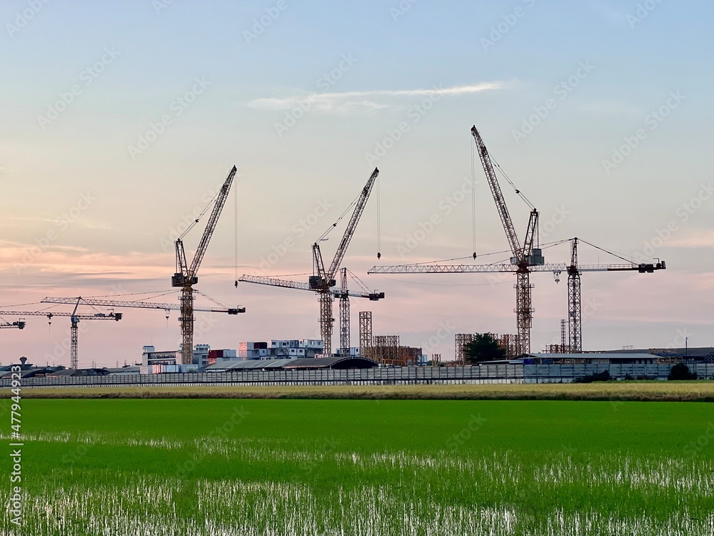 Silhouettes of construction cranes and unfinished residential building on sunrise background. Housing construction, apartment block in winter city. Tower crane on a construction site at sunrise. Silhouettes of construction cranes and unfinished residential building on sunrise background. Housing construction, apartment block in winter city. Tower crane on a construction site at sunrise.