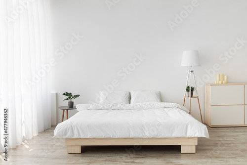 Ideas for scandinavian minimalist bedroom. Double bed with pillows, soft white blanket, lamp and furniture photo