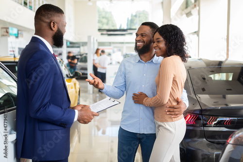 Family Buying Car. African American Spouses Purchasing New Vehicle In Dealership Center