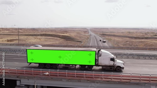 Truck with semi-trailer on which green screen passes over bridge on highway, aerial view. Truck with semi-trailer which chromakey, rides freeway