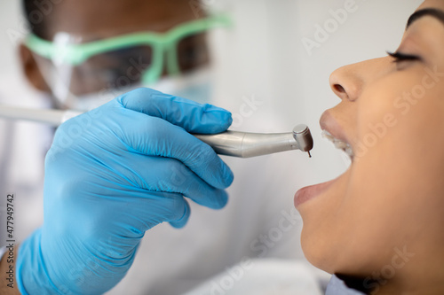 Black Dentist Using Dental Drill During Treatment With Female Patient In Clinic