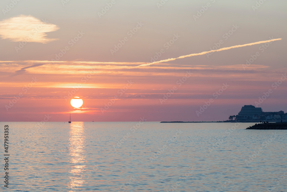 A scenic sunset is reflected in the Mediterranean Sea, with the city of Sitges in the background. A scenic sunset is reflected in the Mediterranean Sea, with the city of Sitges in the background.
