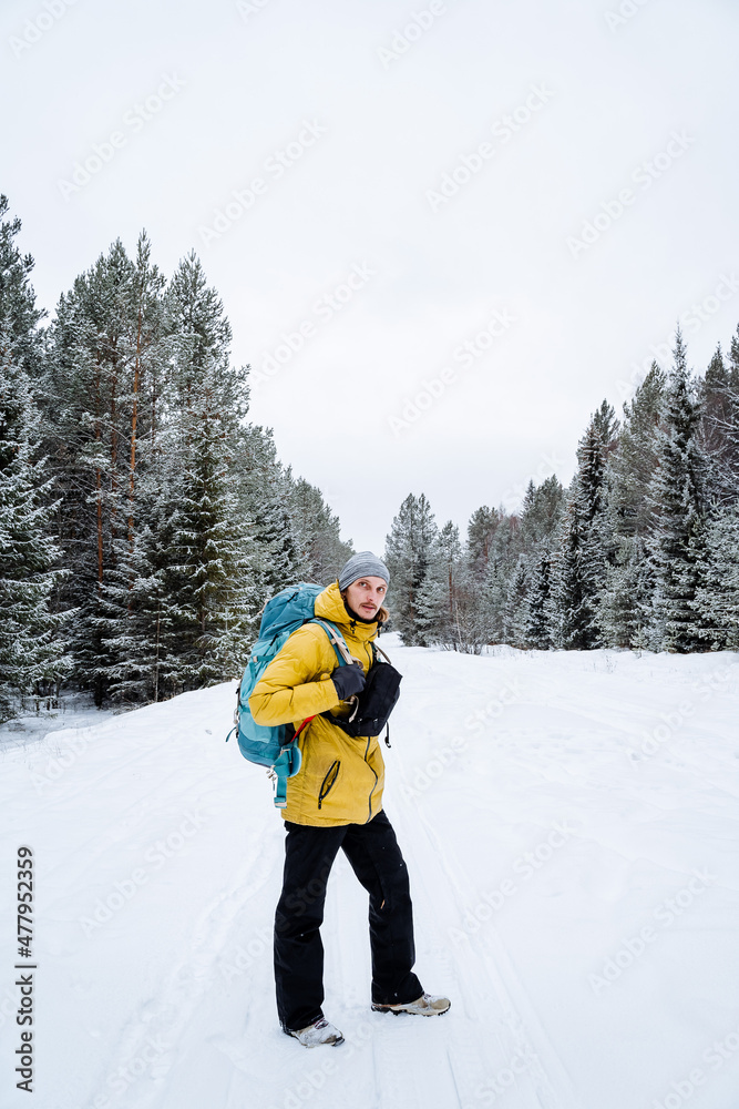 joyful traveler with a bright backpack walks through the forest expanses. Snowy forest and rocks. Climbing the mountain in winter. Survival in the wild.