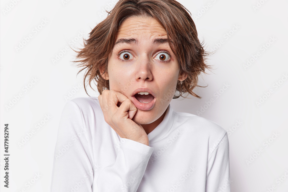 Headshot of frightened impressed woman with dark short hair holds breath from amazement keeps jaw dropped hears something shocking dressed casually isolated over white background. Omg concept Headshot of frightened impressed woman with dark short hair holds breath from amazement keeps jaw dropped hears something shocking dressed casually isolated over white background. Omg concept