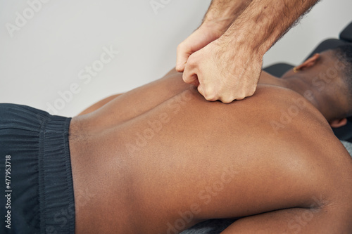 Masseur kneading man thoracic spine muscles with clenched hands