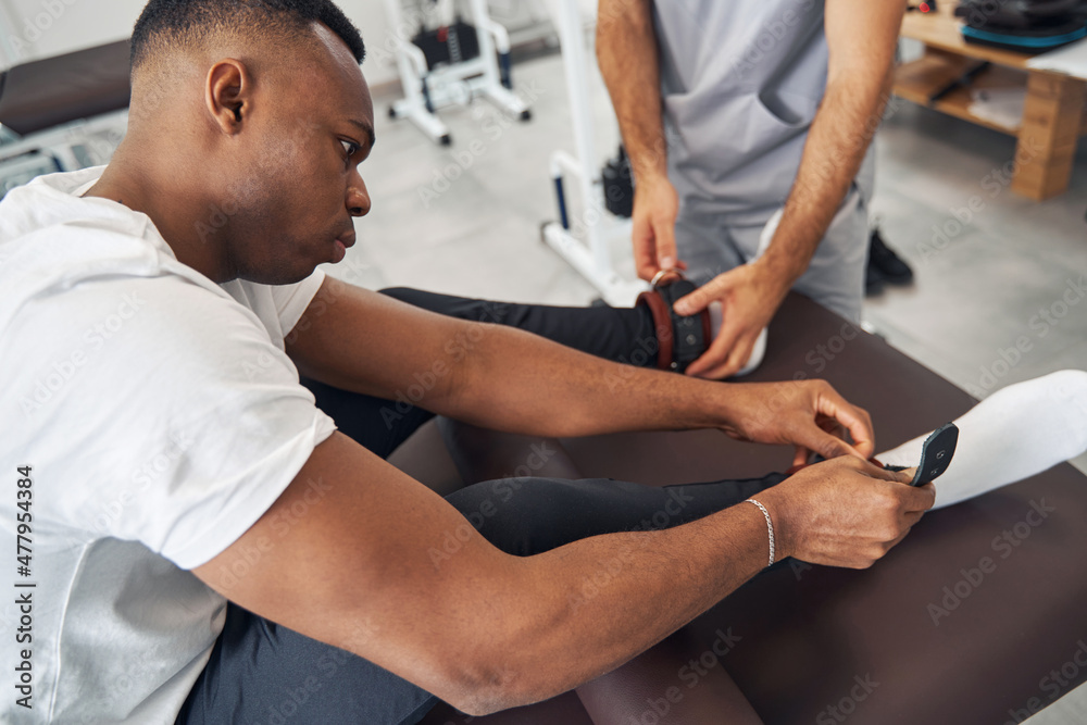 Man putting weights on his ankles assisted by physiotherapist Man putting weights on his ankles assisted by physiotherapist