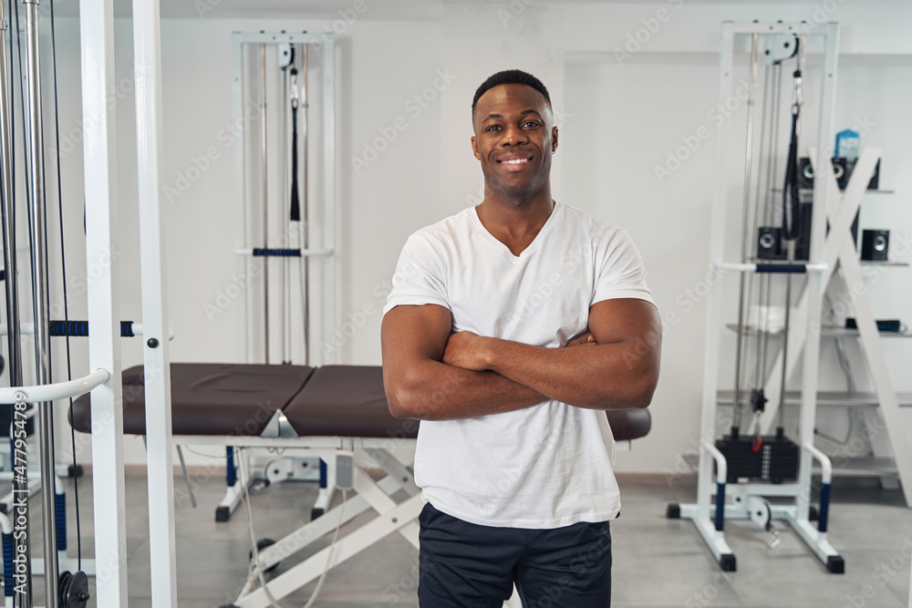 Pleased male athlete posing for camera against fitness equipment Pleased male athlete posing for camera against fitness equipment