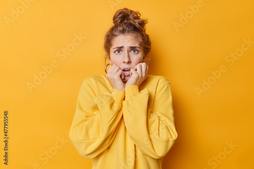 Canvastavla Concerned anxious European woman trembles from fright grabs face stands shocked indoor notices something horrified dressed in jumper isolated over yellow background