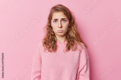 Canvas Print Upset gloomy blue eyed woman has pity look feels discontent and offended looks dissatisfied pouts lips dressed in casual jumper isolated over pink background expresses sadness