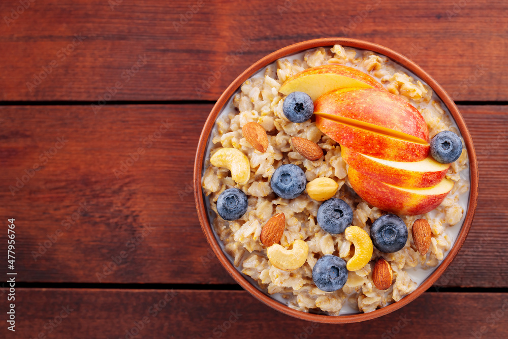 Oatmeal with blueberries, apple and nuts. Bowl of oatmeal porridge on wooden boards. Healthy breakfast concept. Top view. Copy space Oatmeal with blueberries, apple and nuts. Bowl of oatmeal porridge on wooden boards. Healthy breakfast concept. Top view. Copy space