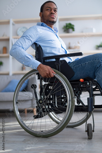 Sad disabled young man in wheelchair feeling alone and depressed at home, low angle view