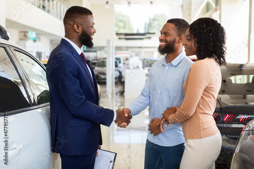 Sales Manager Helping Black Couple Choose New Car In Modern Dealership Center