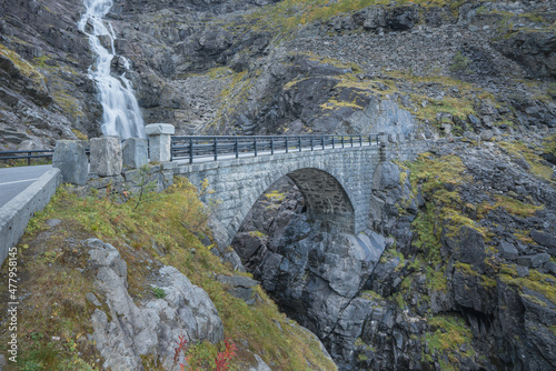 Narrow stone bridge on the serpentine of famous mountain road Troll Stigen, or Trollstigen, in Norway. Stigfossen waterfall in the back. photo