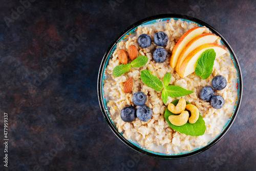 Oatmeal with blueberry, almonds and cashew nuts on a dark background. Oatmeal porridge bowl with apples and mint leaves. Top view. Copy space