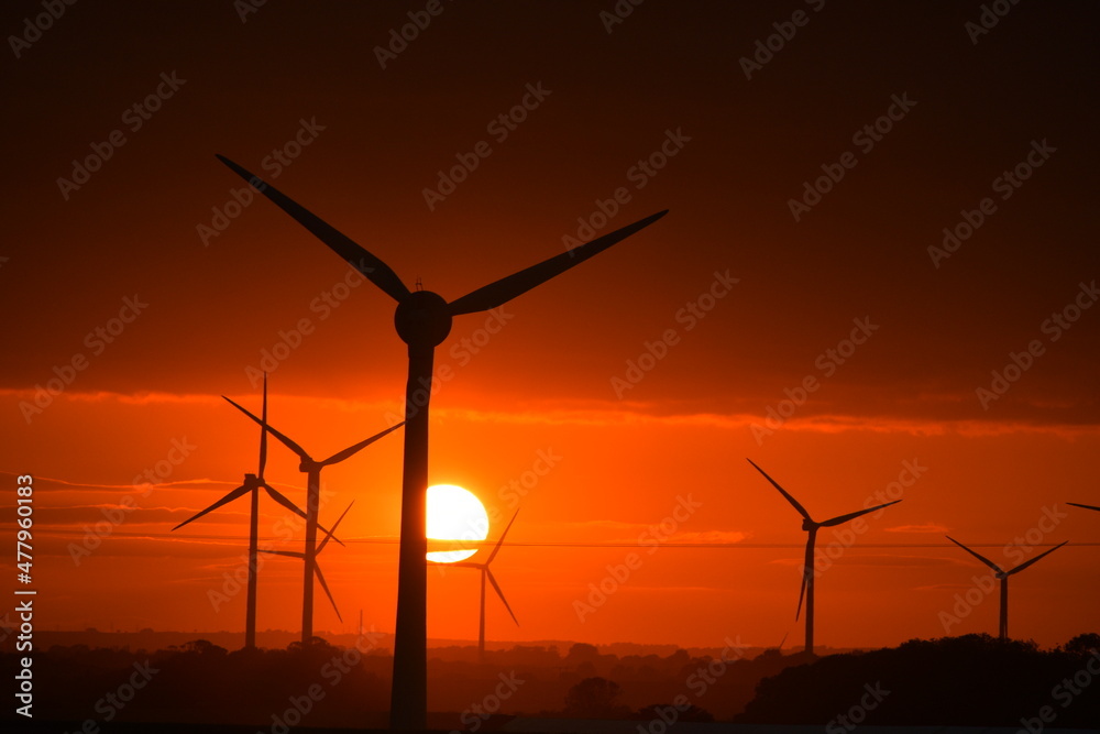 Deep orange sunset falls behind a field of giant wind turbines Deep orange sunset falls behind a field of giant wind turbines